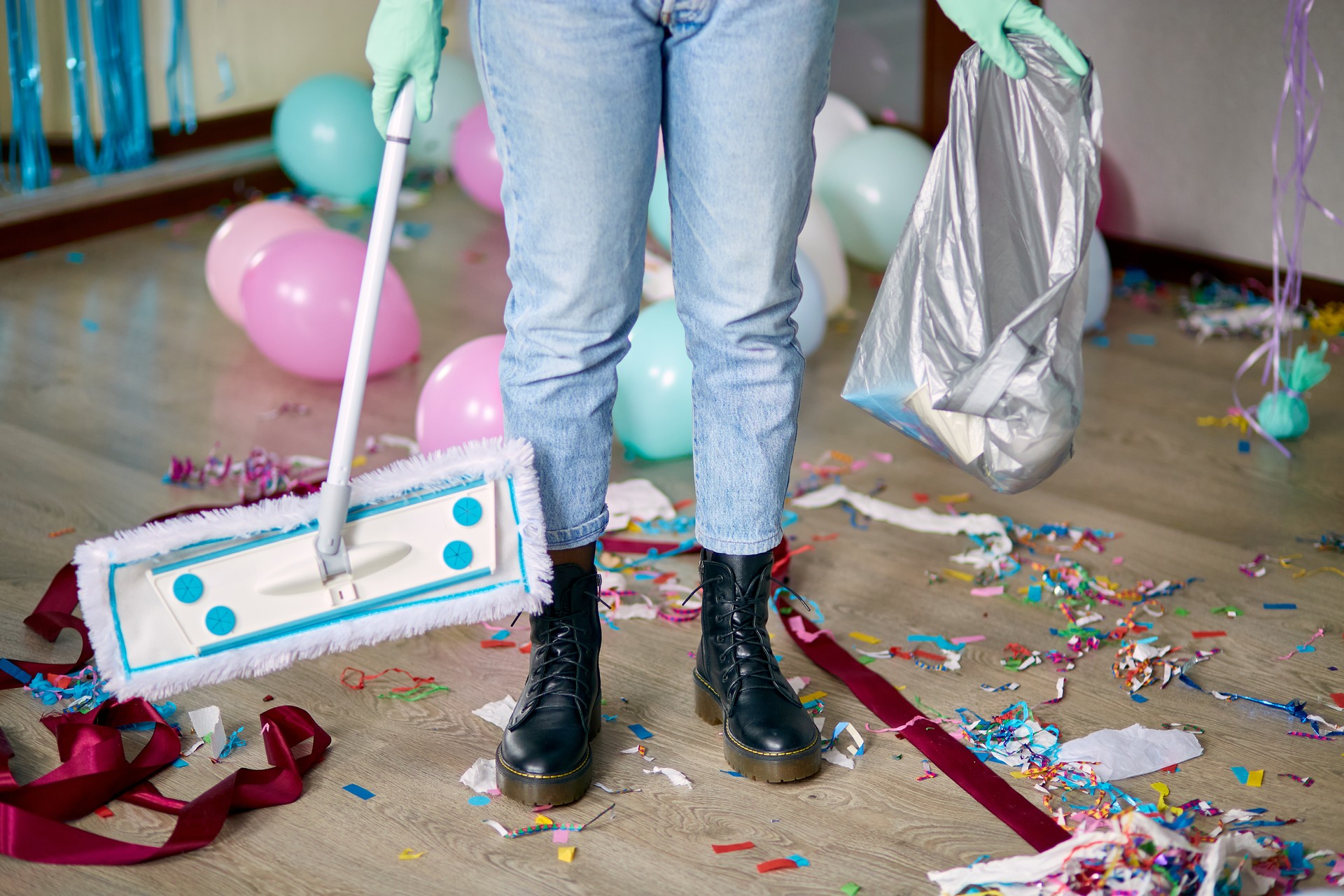 Woman with pushbroom cleaning mess of floor in room after party confetti