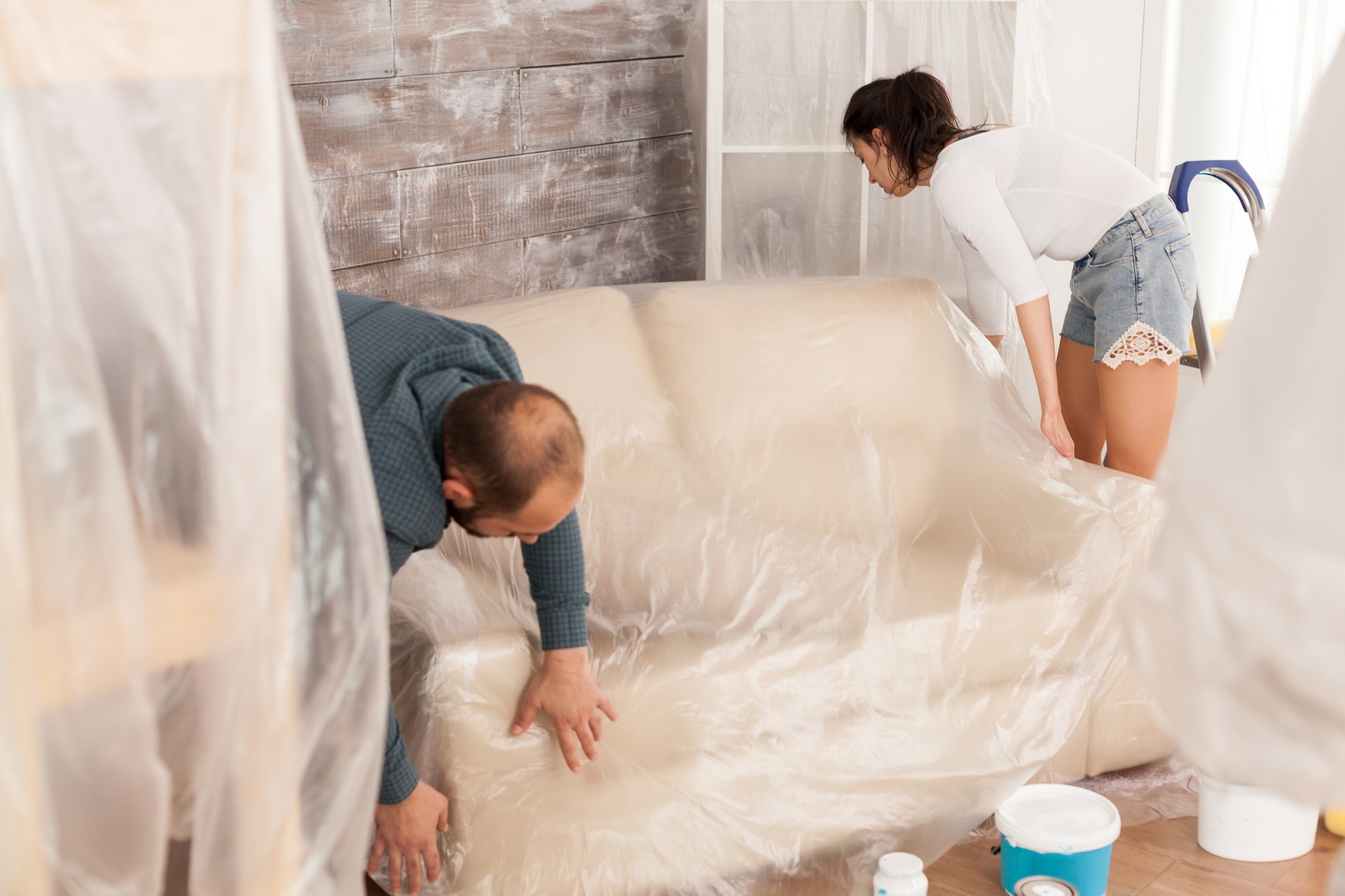 Couple wrapping sofa in plastic foil